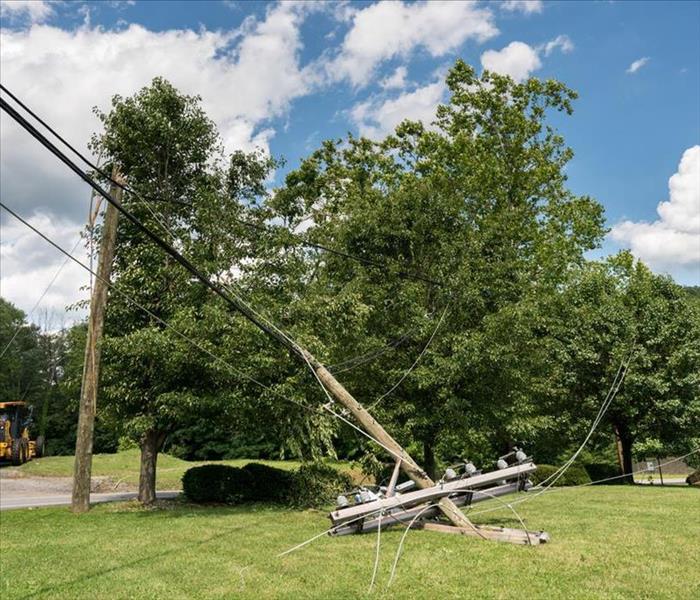 Broken snapped wooden power line post with electrical components on the ground after a storm