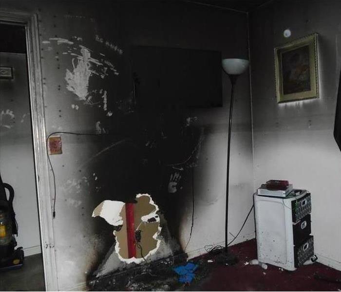 A wall from the living room has a big hole and is black due to fire in the home