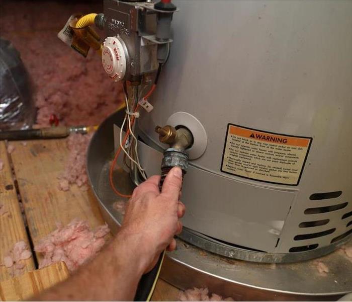 A Hand attaching the hose to a home water heater